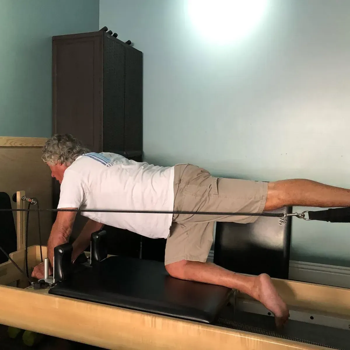 Two women doing Pilates side plank exercises on reformers in a bright studio