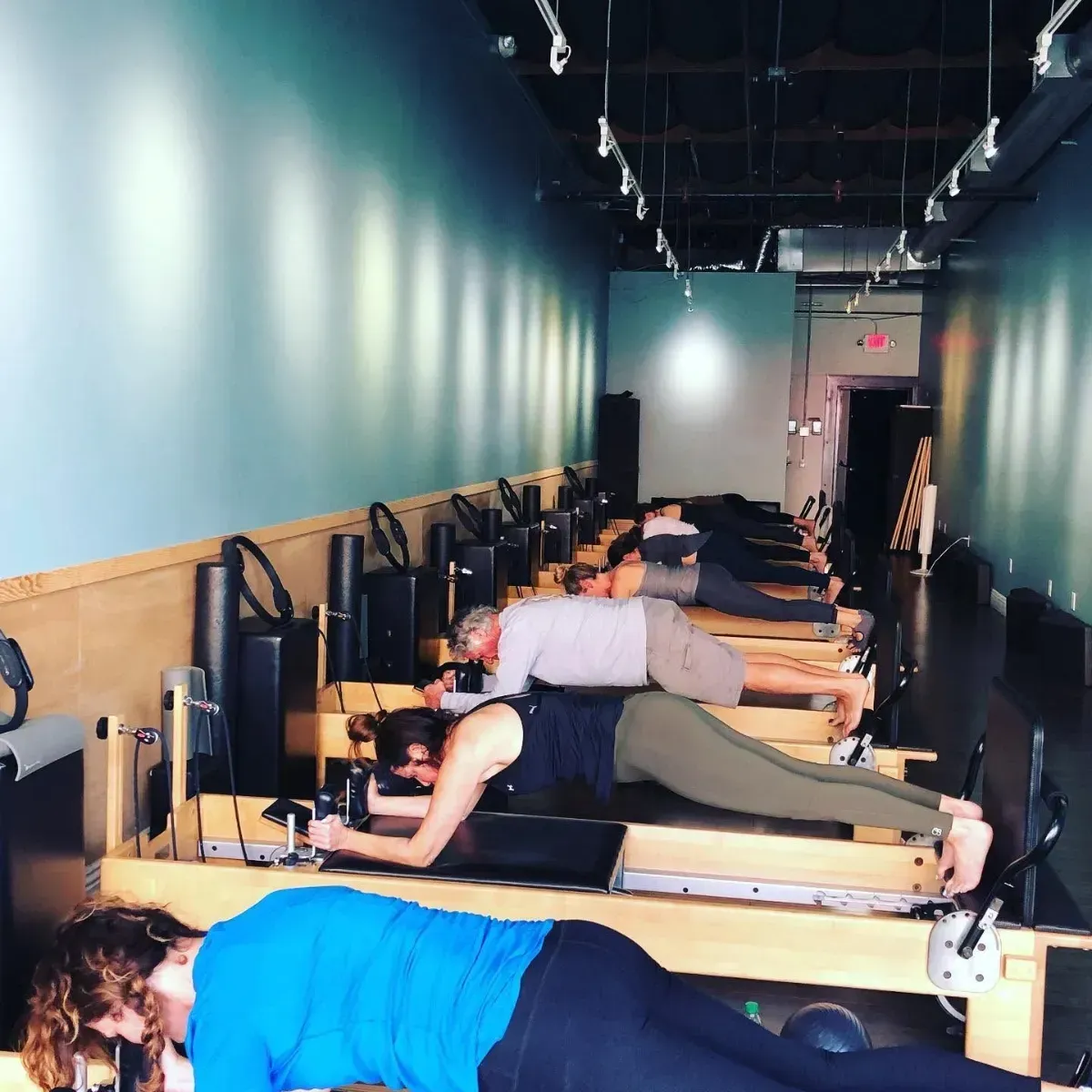 Woman balancing on one leg in a Pilates studio, holding a barre with outstretched arms.