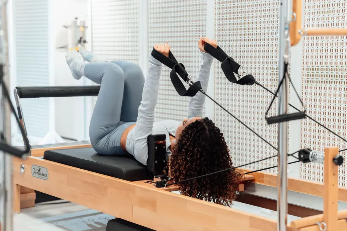 Two people exercising on reformer machines in a long studio hallway