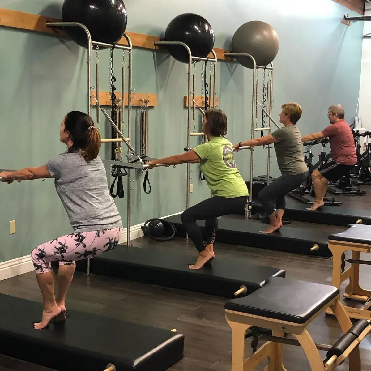 Person on a Pilates reformer in a studio, viewed from behind, with large windows and exercise equipment.