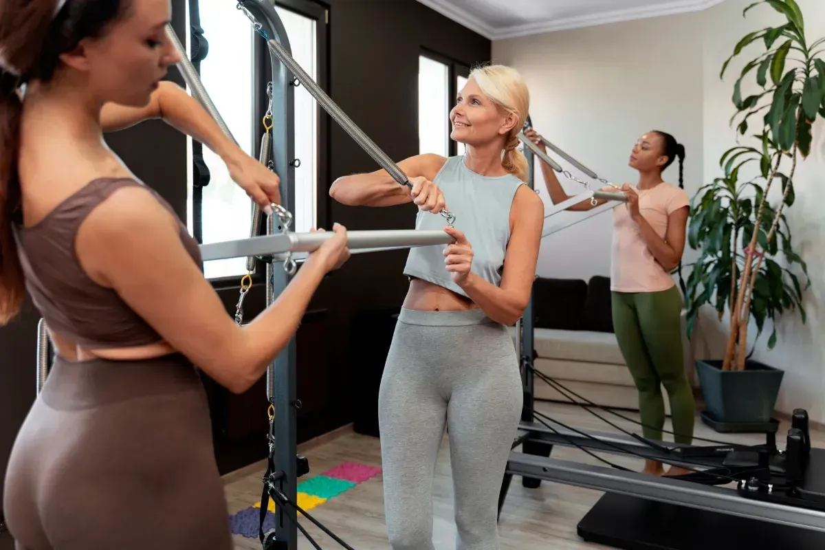 Woman balancing on one leg in a Pilates studio, holding a barre with outstretched arms.