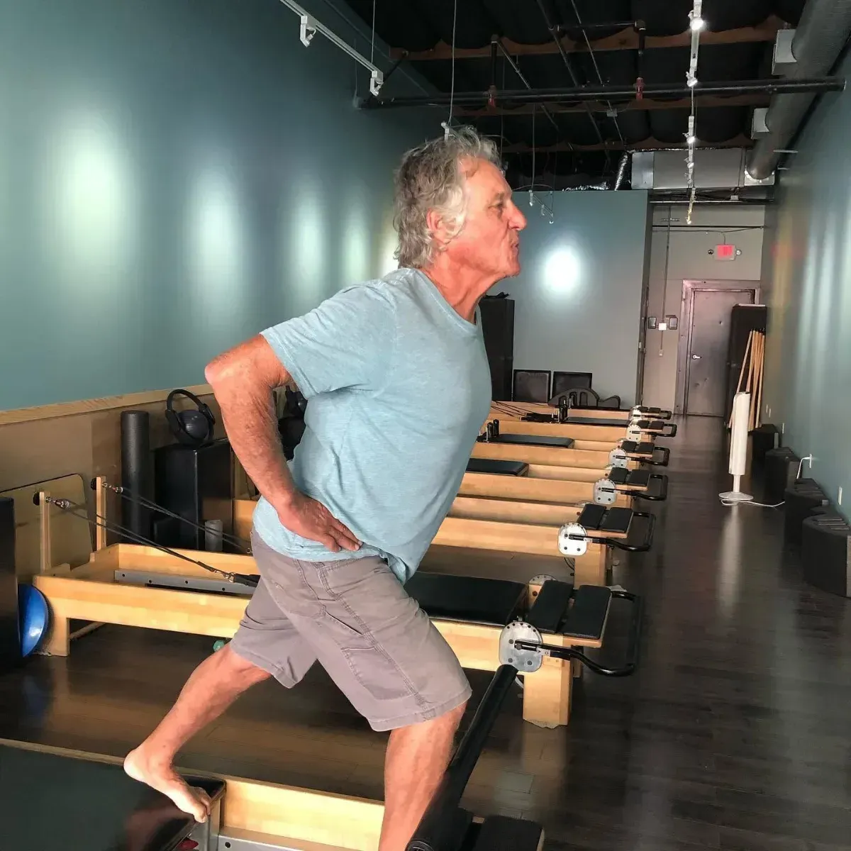 Woman balancing on one leg in a Pilates studio, holding a barre with outstretched arms.