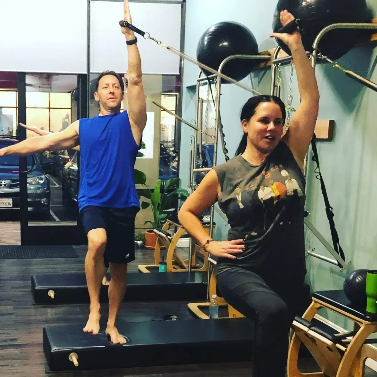Two women doing Pilates side plank exercises on reformers in a bright studio