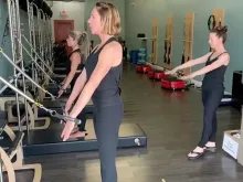 Three women using suspension straps in a fitness studio, standing and leaning back during a workout.