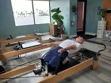 Person lying on a Pilates reformer in a bright studio, stretching back with arms extended