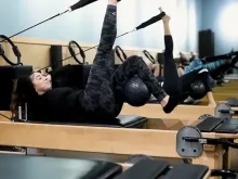 People exercising on Pilates reformers in a studio, doing leg lifts with resistance straps