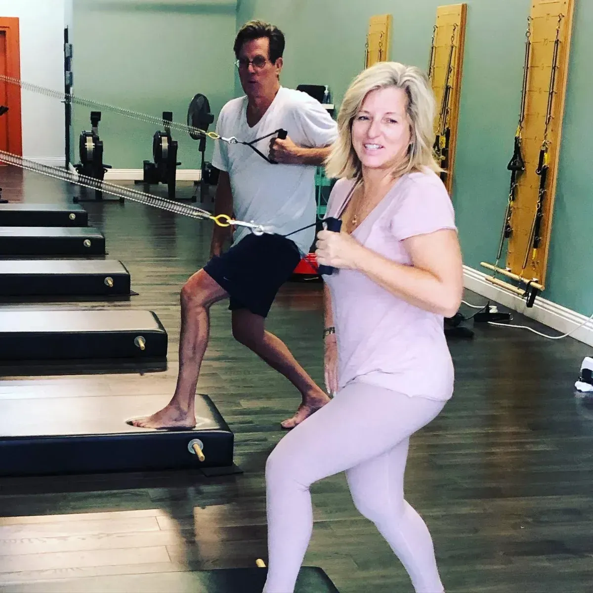 Two people exercising on reformer machines in a long studio hallway