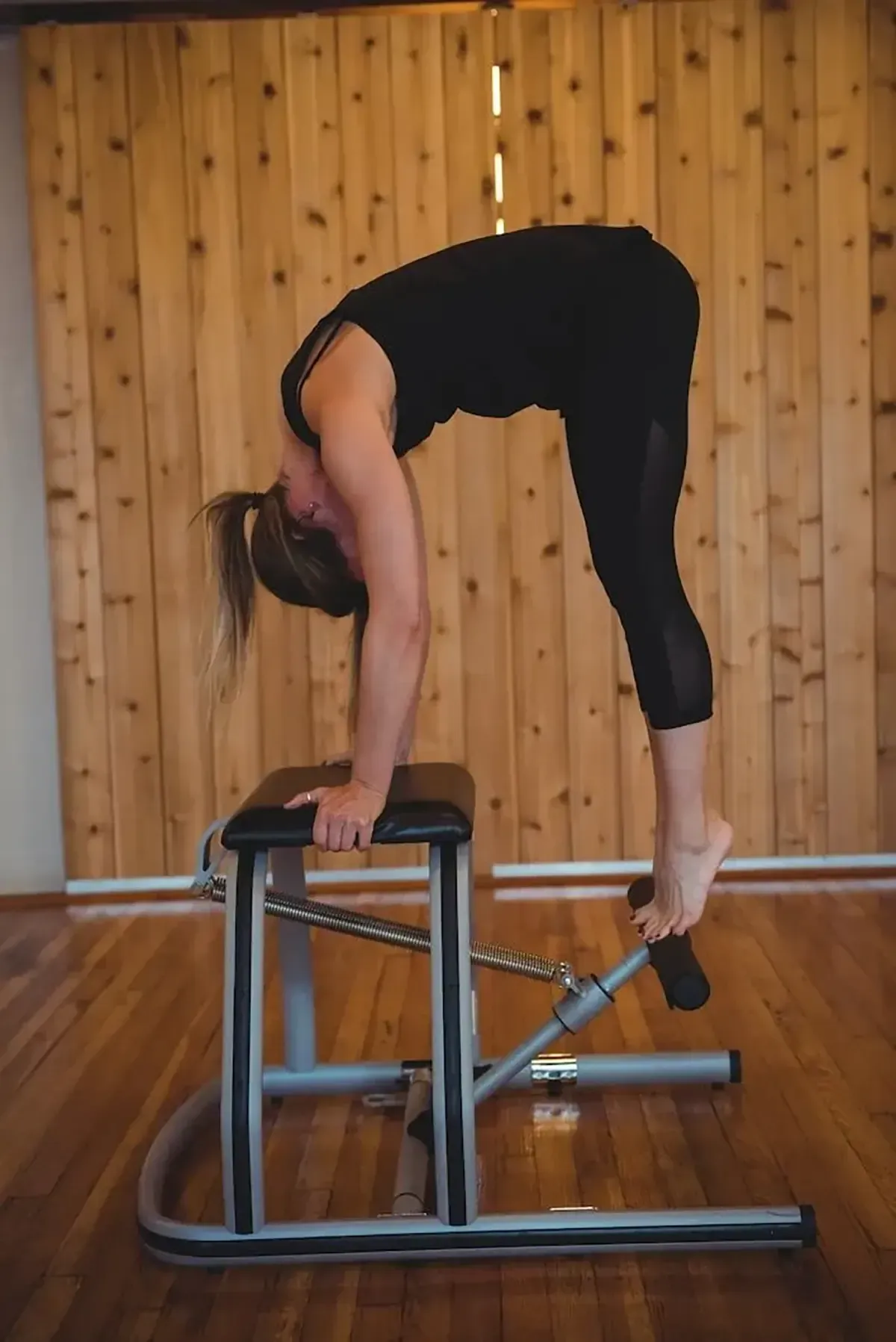 Two women doing Pilates side plank exercises on reformers in a bright studio