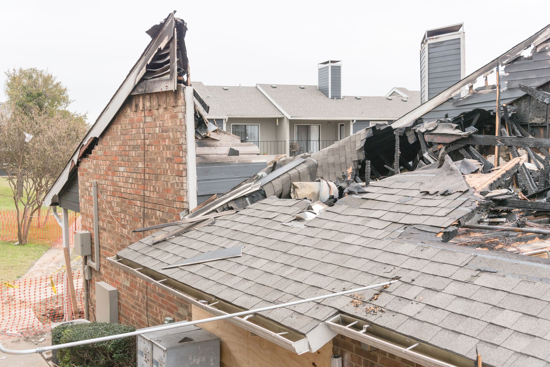 Damaged roof and brick house after fire, with collapsed shingles and smoke-blackened debris