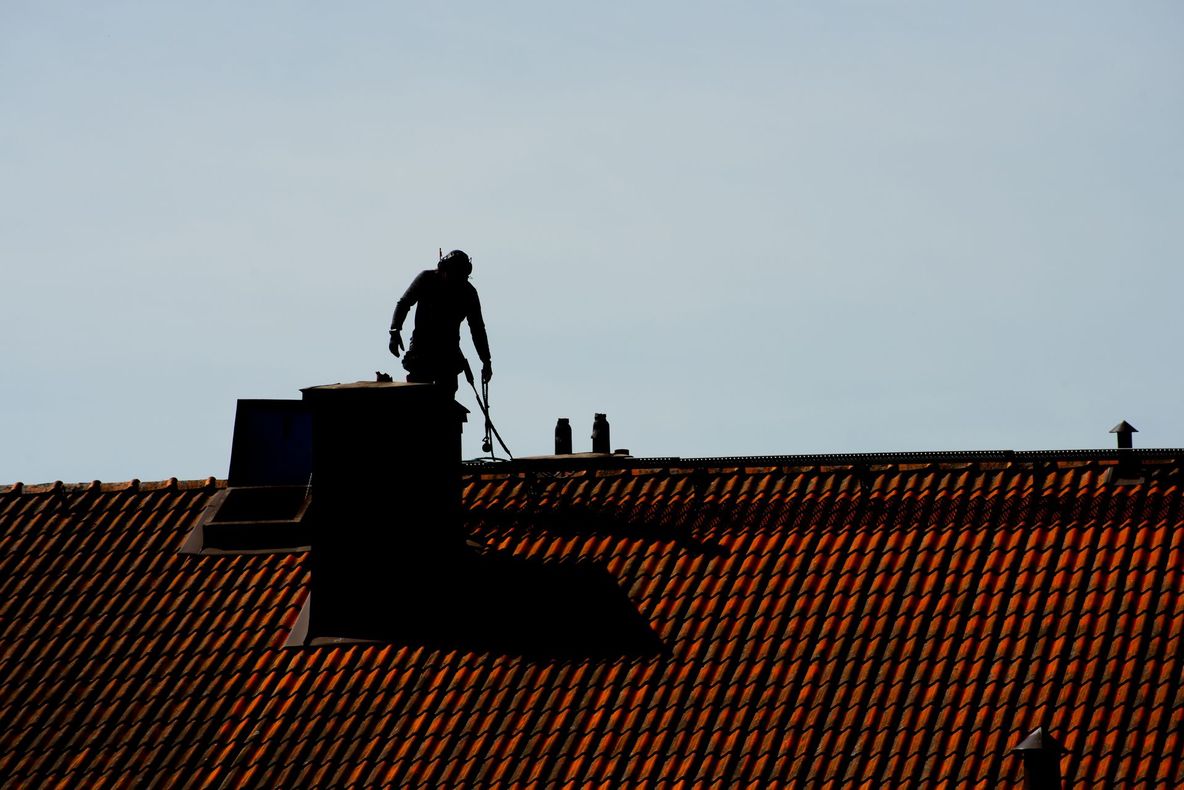 Silhouette of a person on a rooftop above red tiles against a pale sky