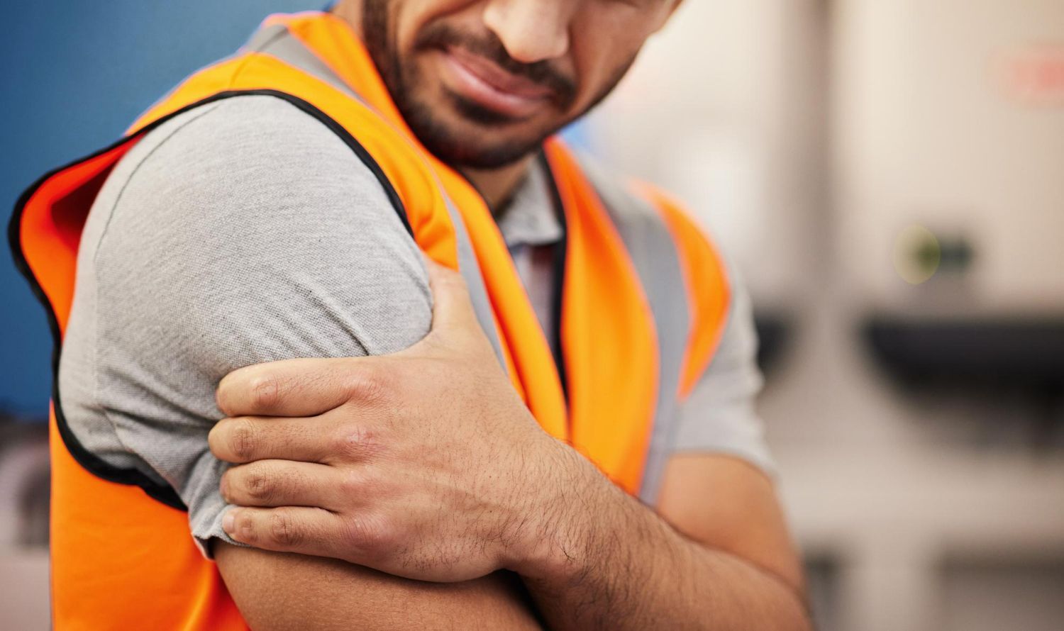 Man in an orange safety vest, holding his arm in pain, likely a workplace injury.