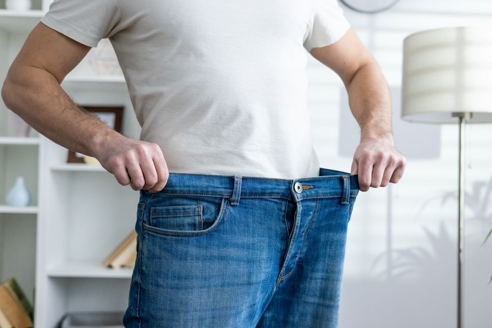 Person holding out oversized blue jeans in a bright room