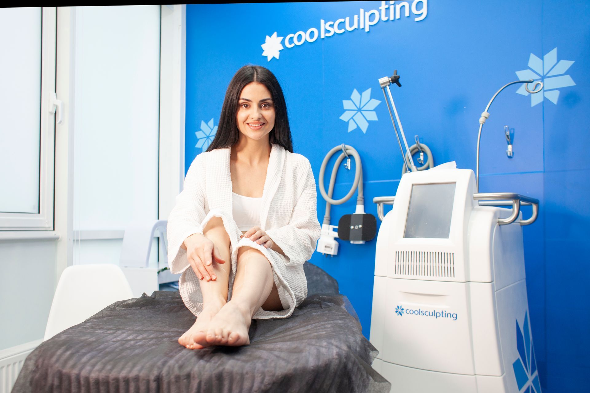 A woman is sitting on a bed in front of a machine.