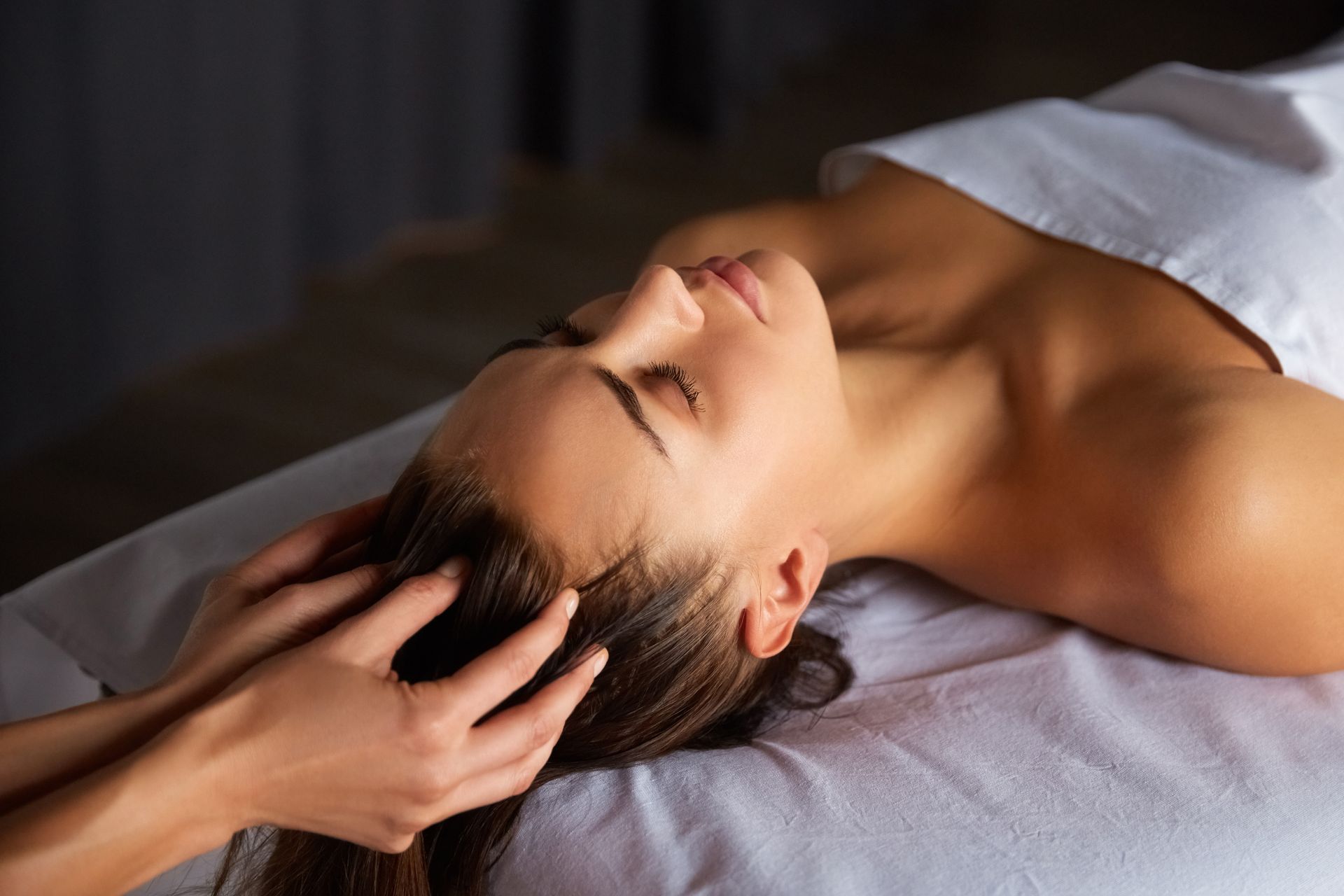 Woman receiving a relaxing head massage on a treatment table, eyes closed, in a spa-like setting
