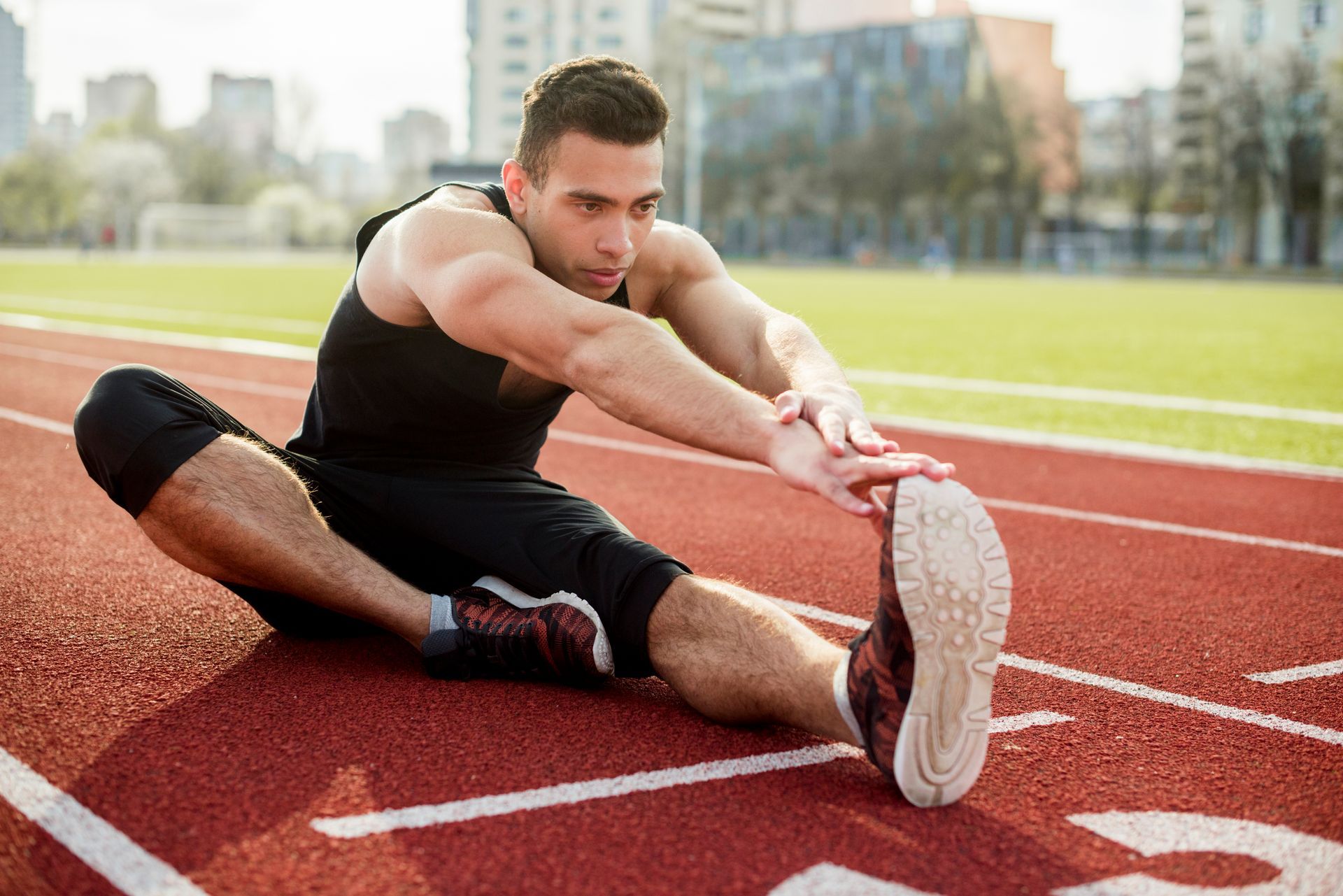 A man is sitting on a track stretching his legs.