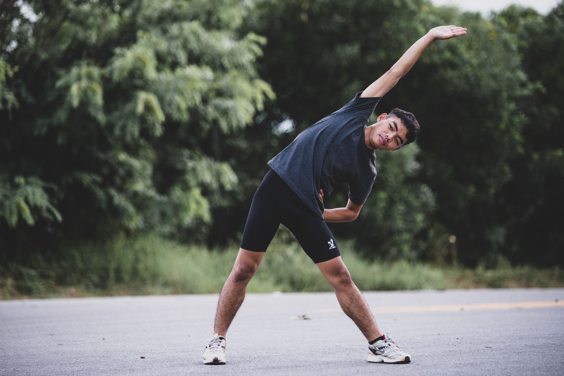 A young man is doing stretching exercises on the side of the road.