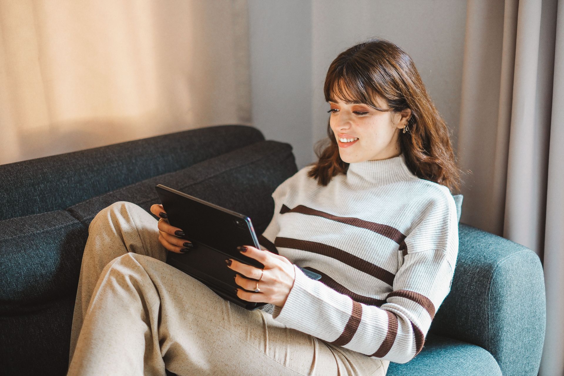 Person reclining on a blue couch, using a tablet in a softly lit room.