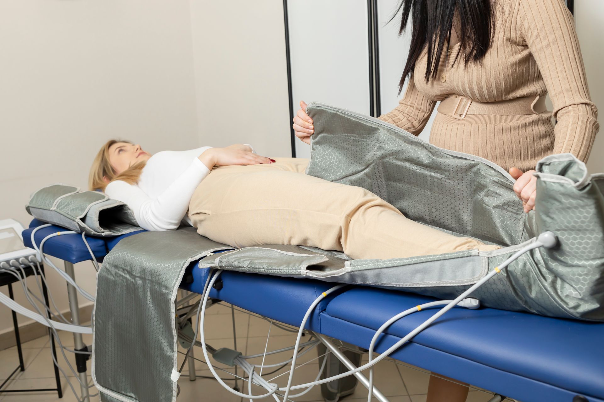 Woman lying on a treatment table while another person adjusts a gray blanket in a clinic setting