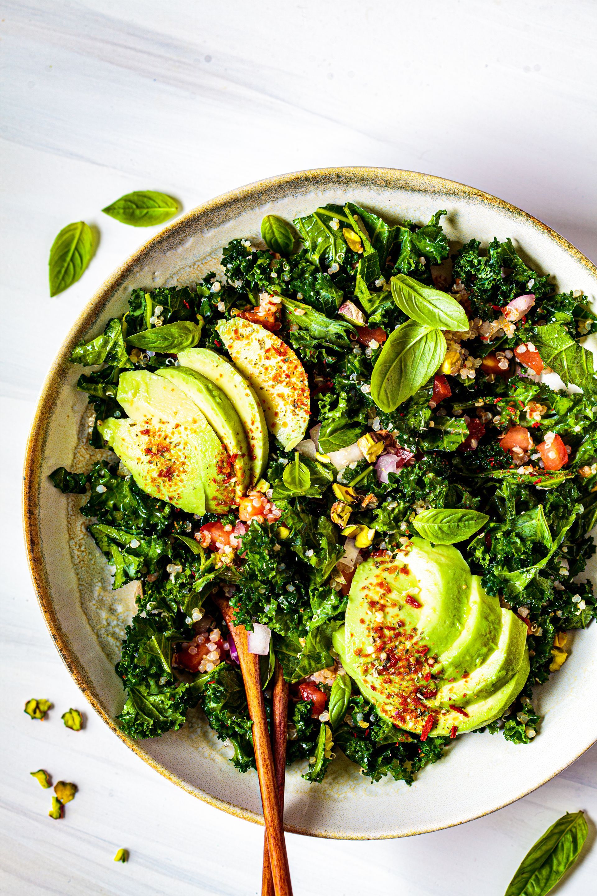 A salad with avocado , kale , tomatoes , and basil in a bowl with chopsticks.