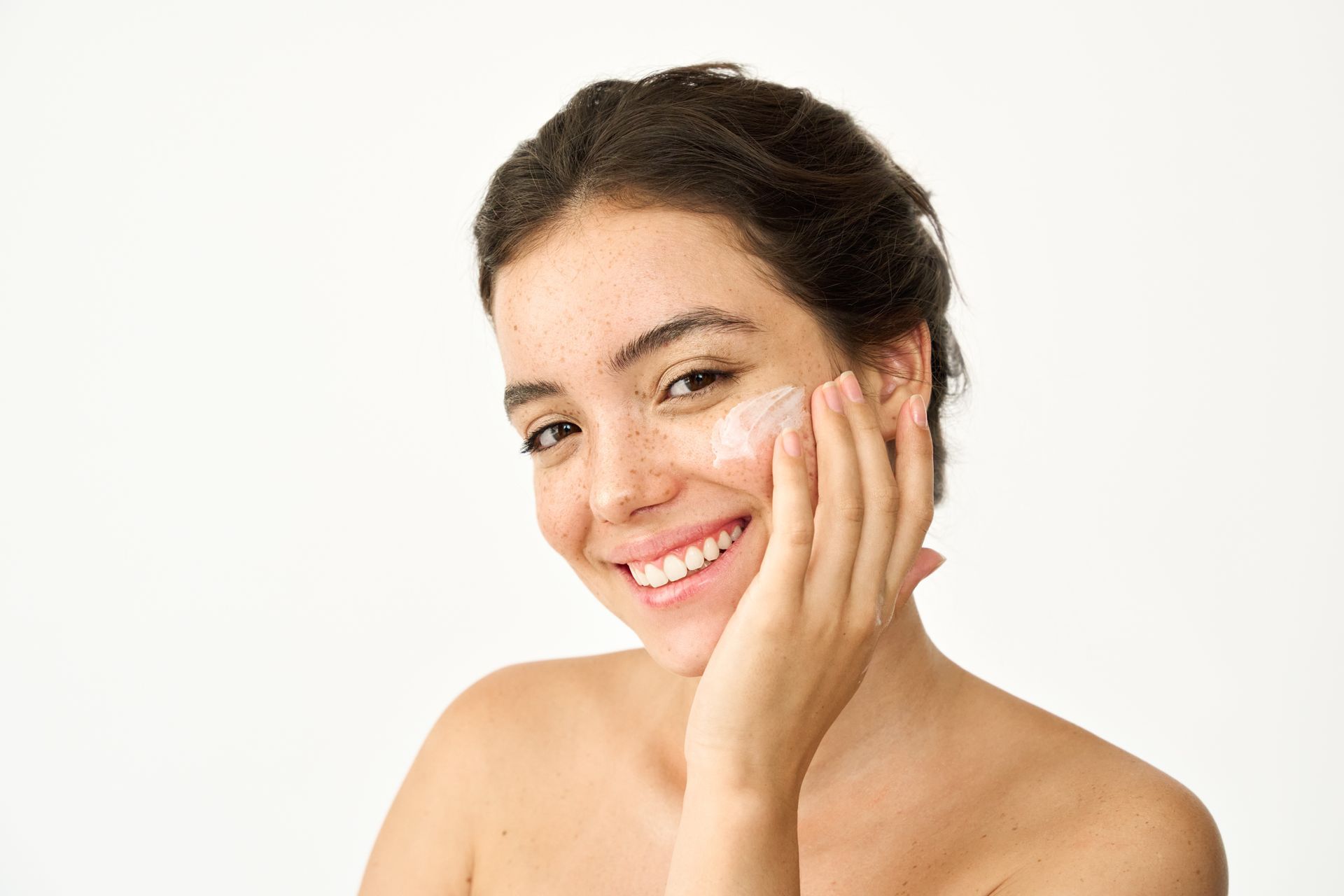 A woman is smiling while applying cream to her face.