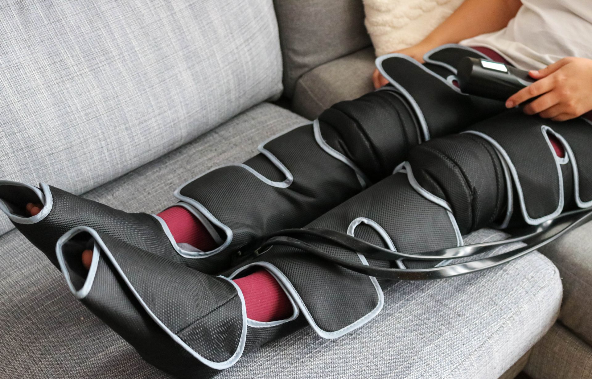 Person using a leg compression device on a couch, black and gray wraps.