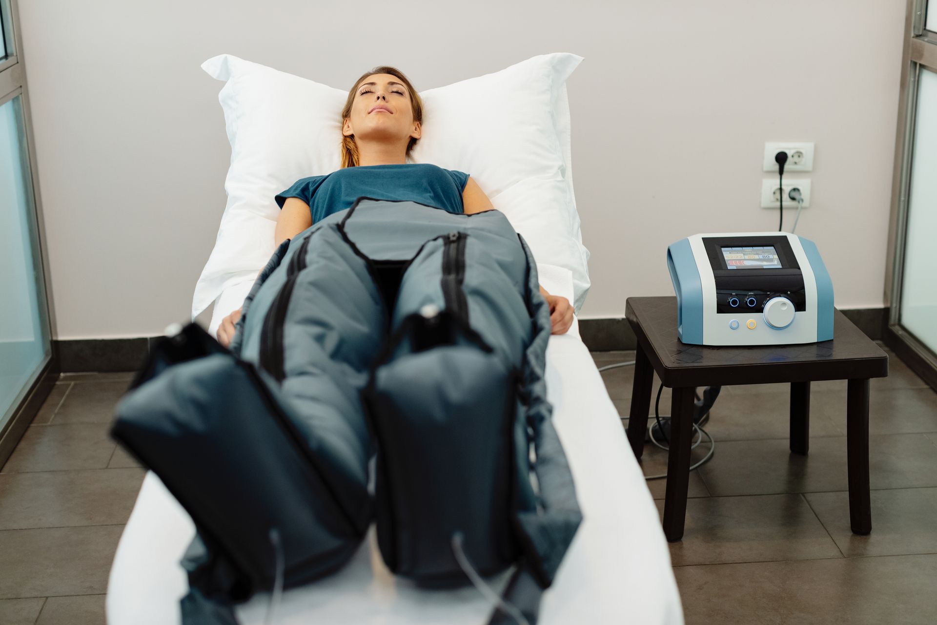 Person lying on a therapy table with compression boots in a clinical room