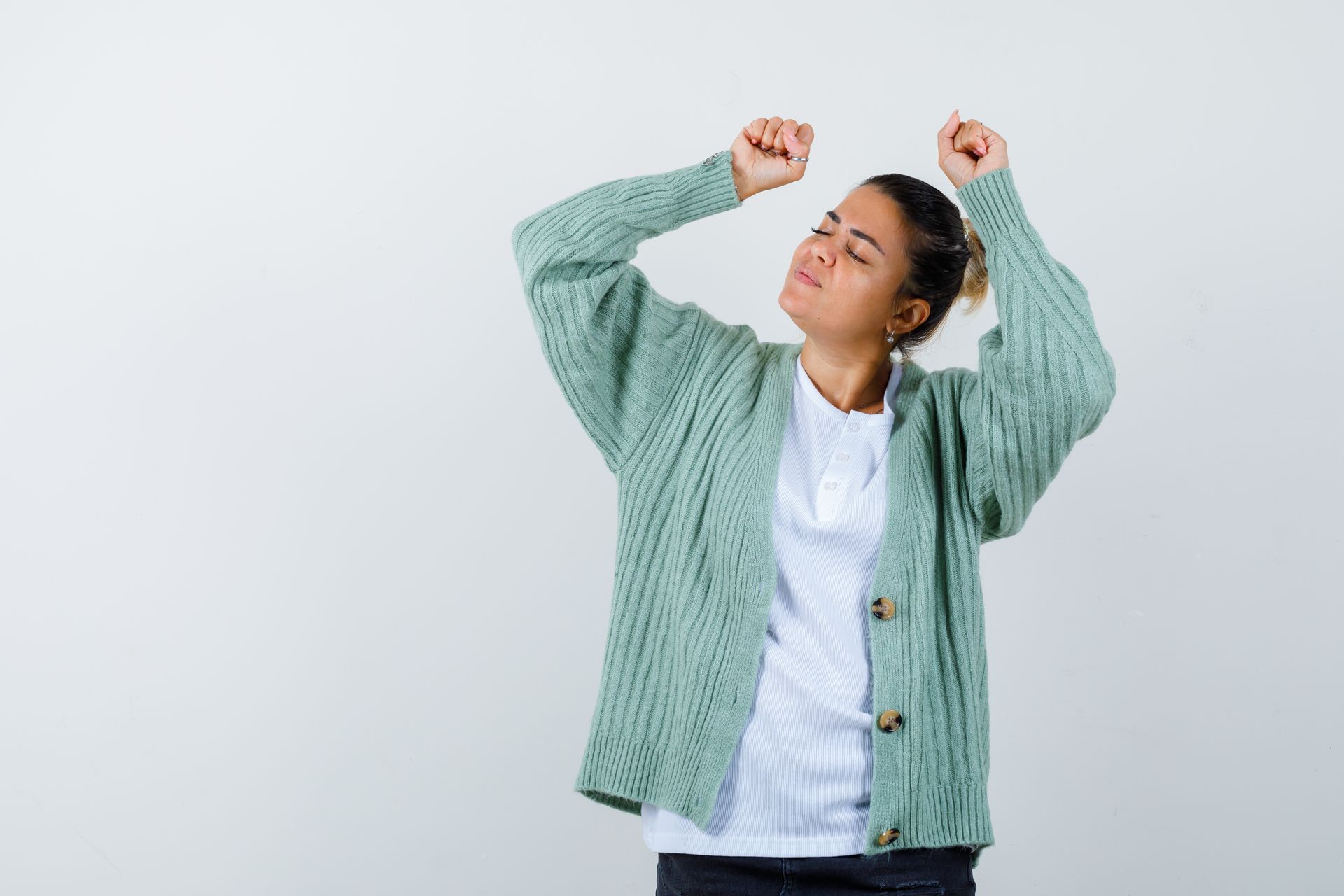 A woman in a green sweater is dancing with her arms in the air.