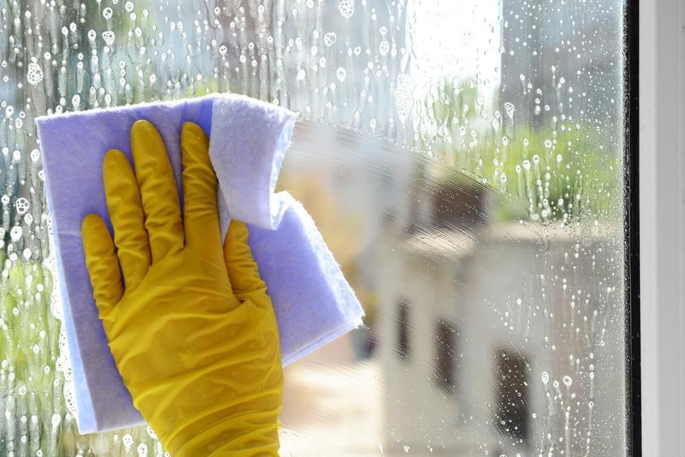 A Person Wearing Yellow Gloves Is Cleaning A Window — Amy's Domestic Agency In Pimlico, QLD