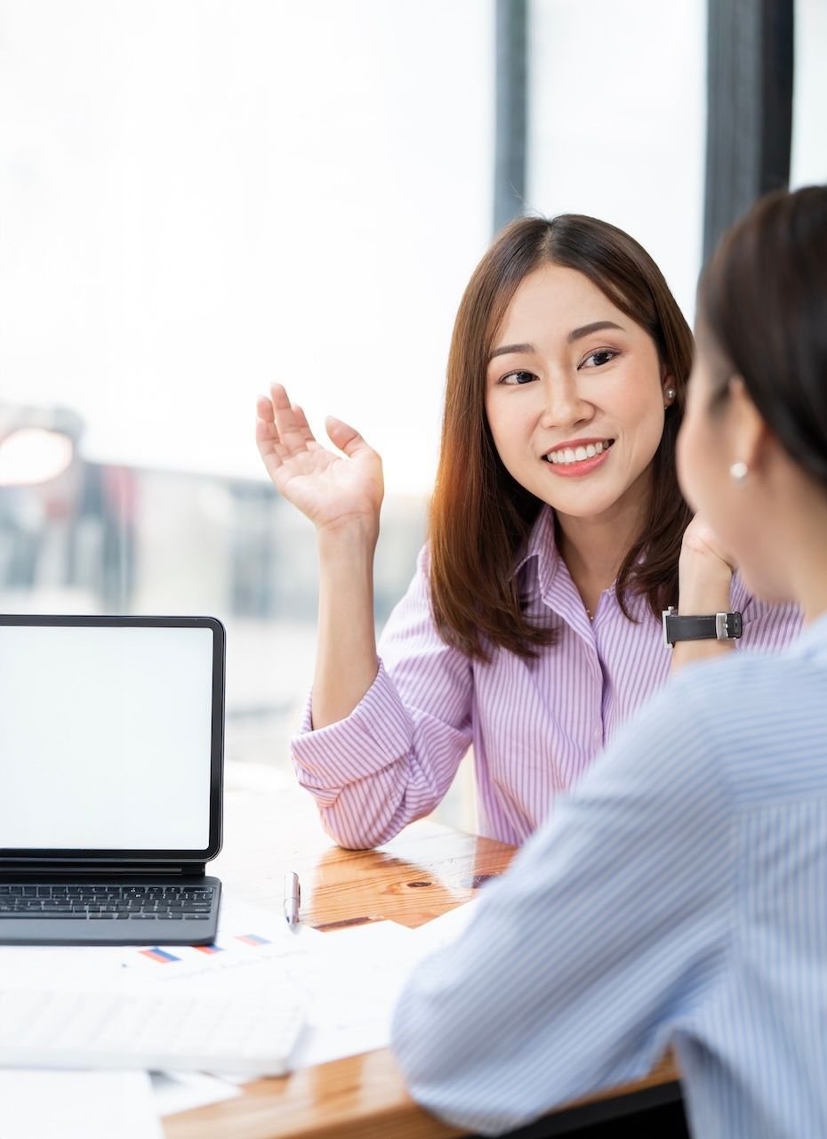 Two people discussing at a desk with a laptop in a bright office