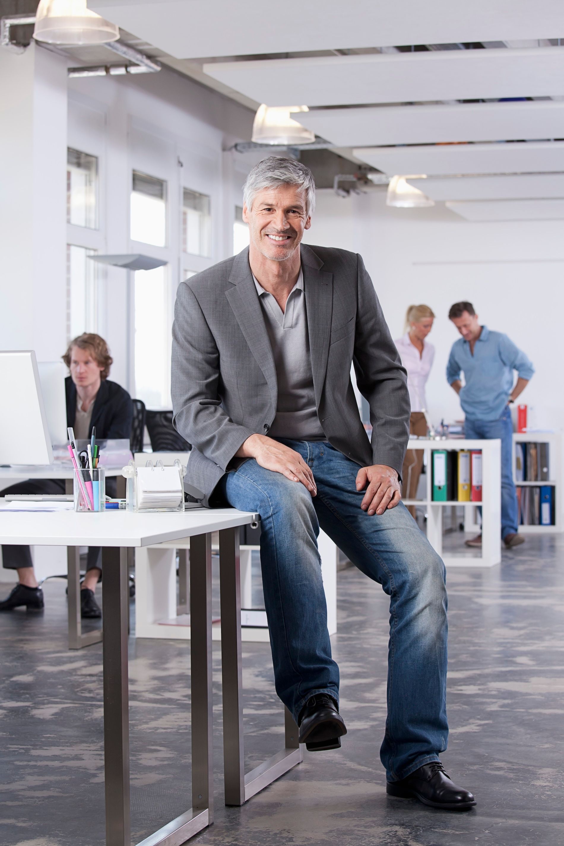 Man sitting on a desk in a bright office with coworkers in the background