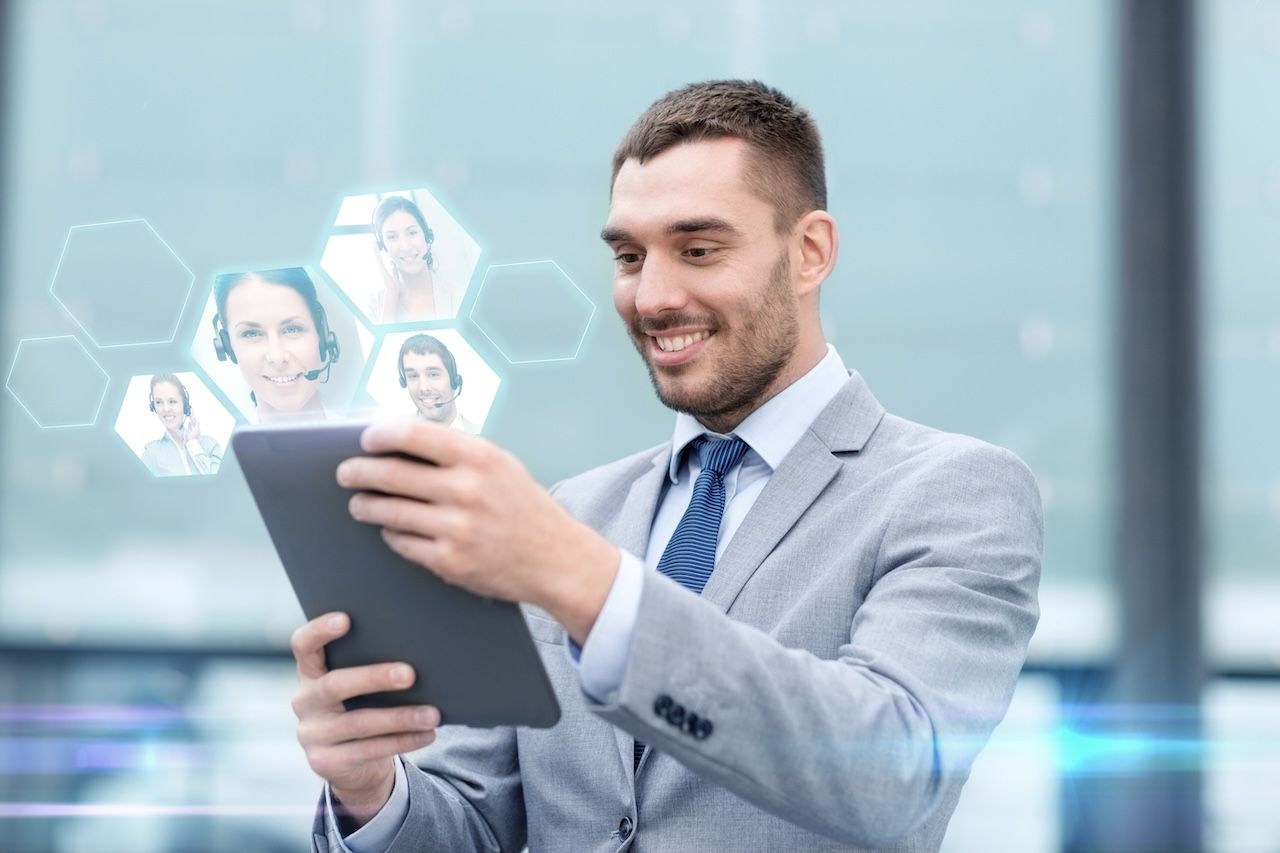 Smiling professional using a tablet in a bright office with virtual video call icons in the background