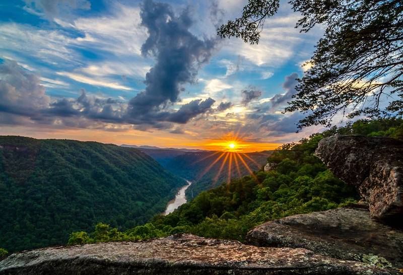 Sunset over a lush green river valley. Golden sunburst through clouds, highlighting the water.