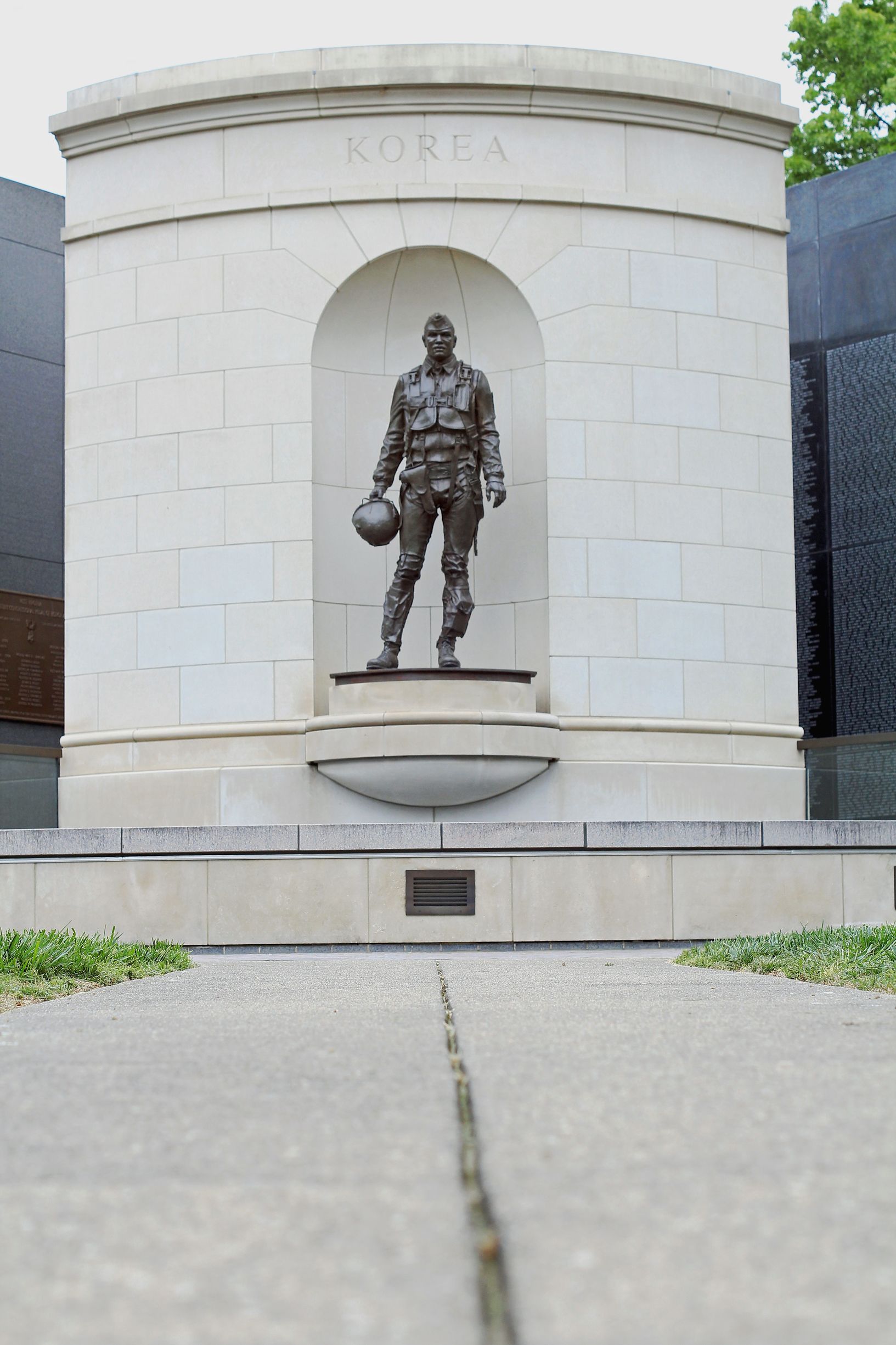 A bronze statue of a pilot holding a helmet stands in an arched alcove at the center of a stone monument.