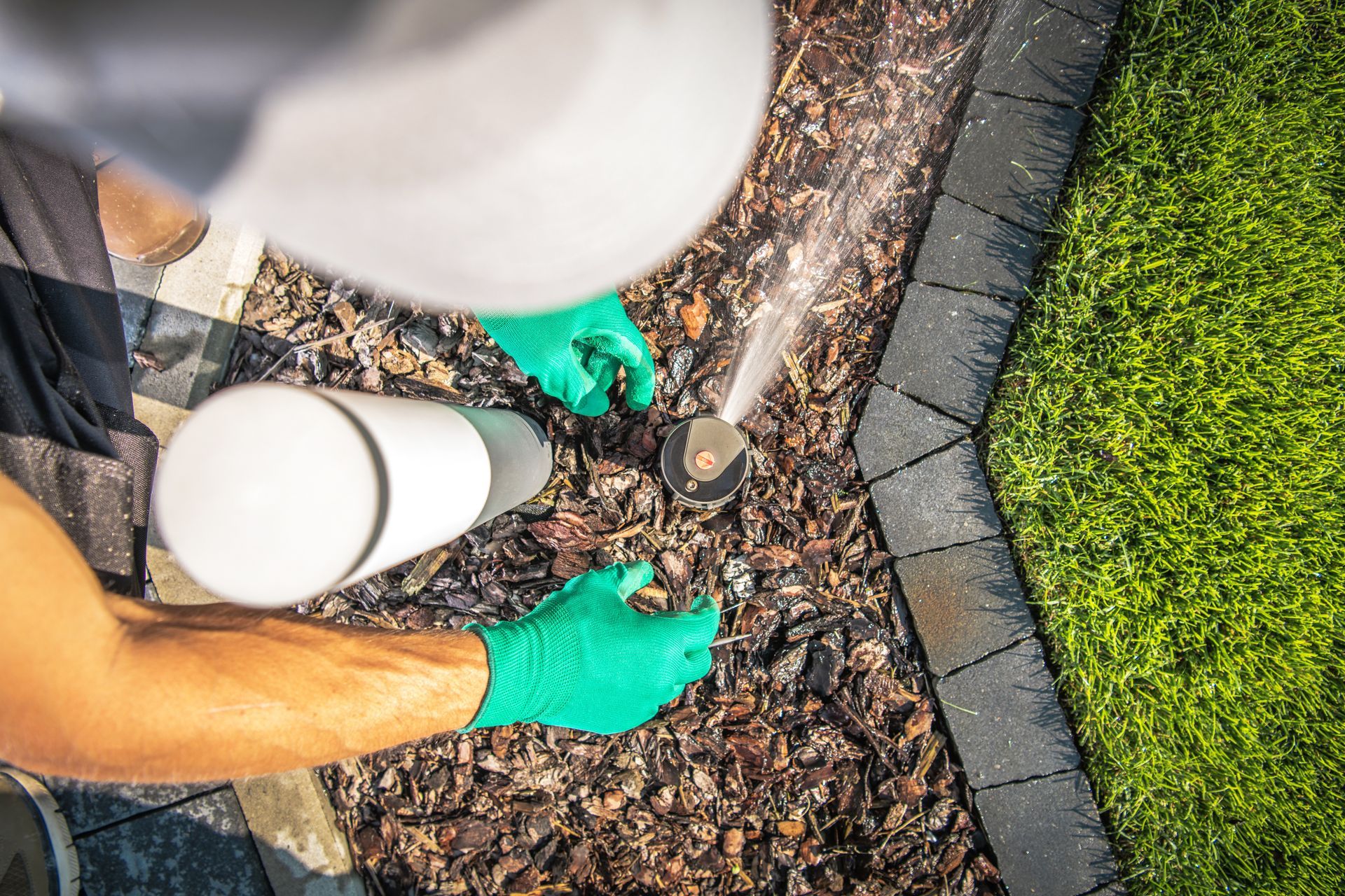 Person in green gloves installing edging in a garden bed beside a lawn