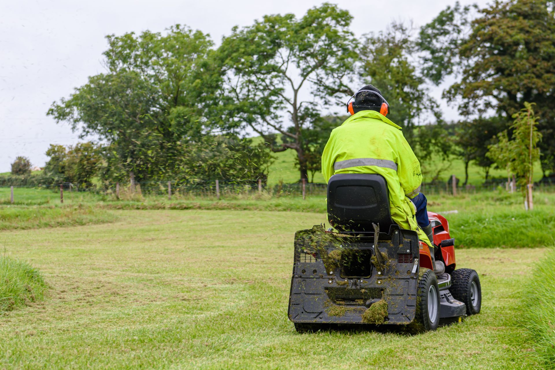 Person on a riding lawn mower cutting grass in a park with trees in the background