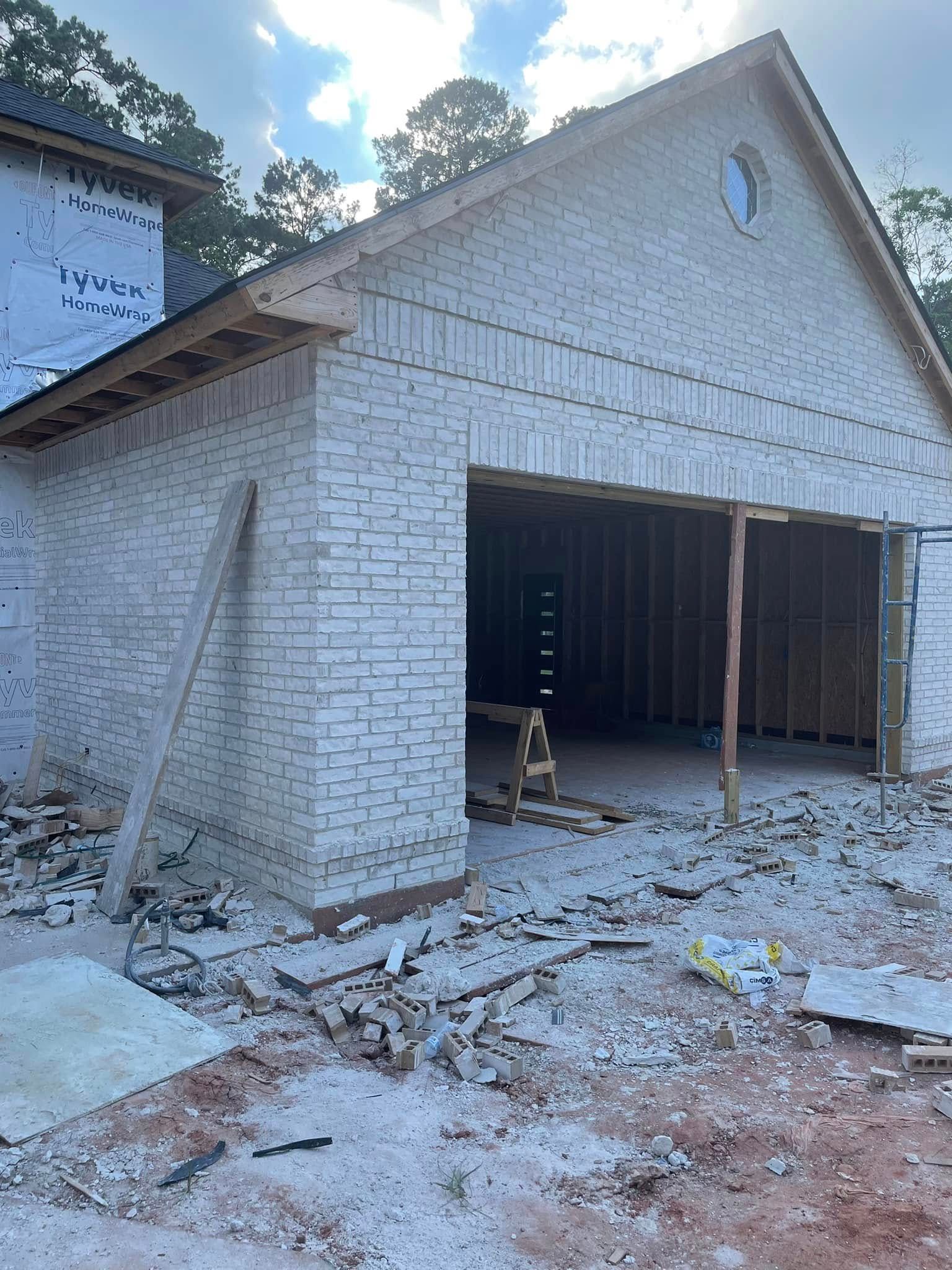 A light-colored brick garage under construction, featuring an arched entryway and a small circular window in the gable.