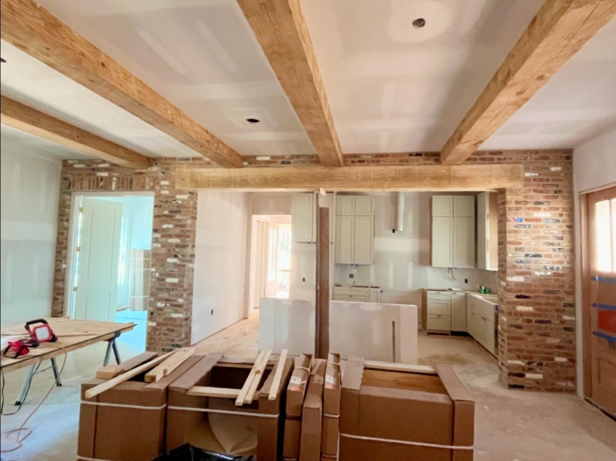 A room under renovation with wooden ceiling beams, exposed brick walls, and cardboard boxes of materials in the center.