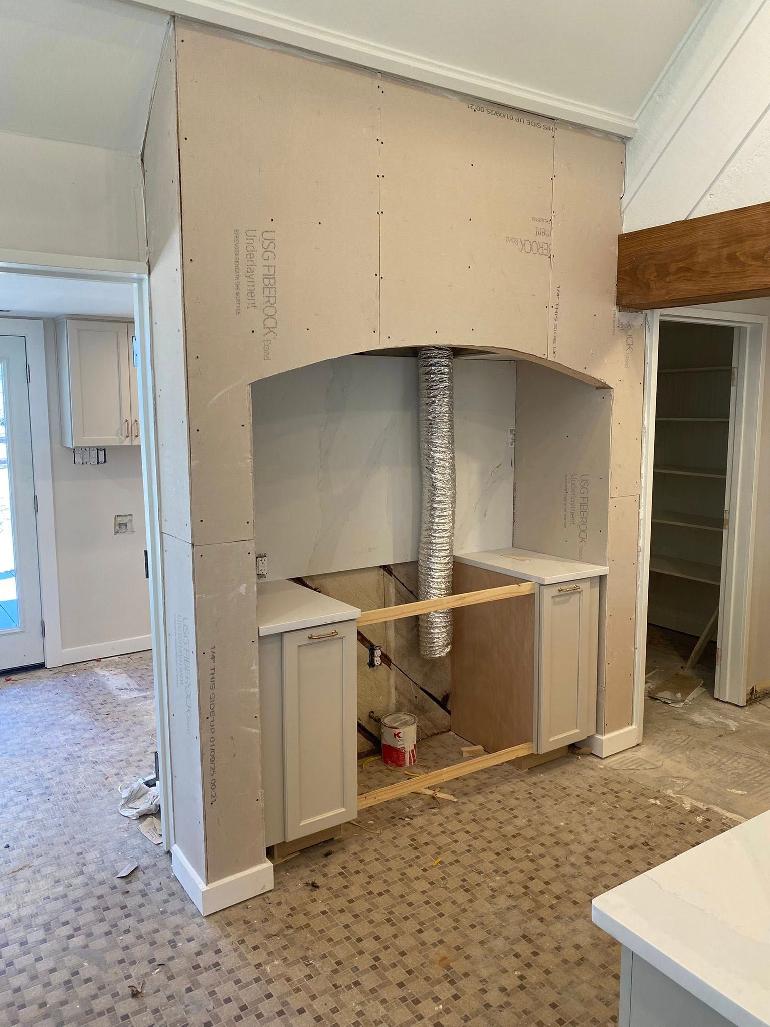 A kitchen under renovation showing a drywall-enclosed range hood structure with base cabinets and vent ducting.