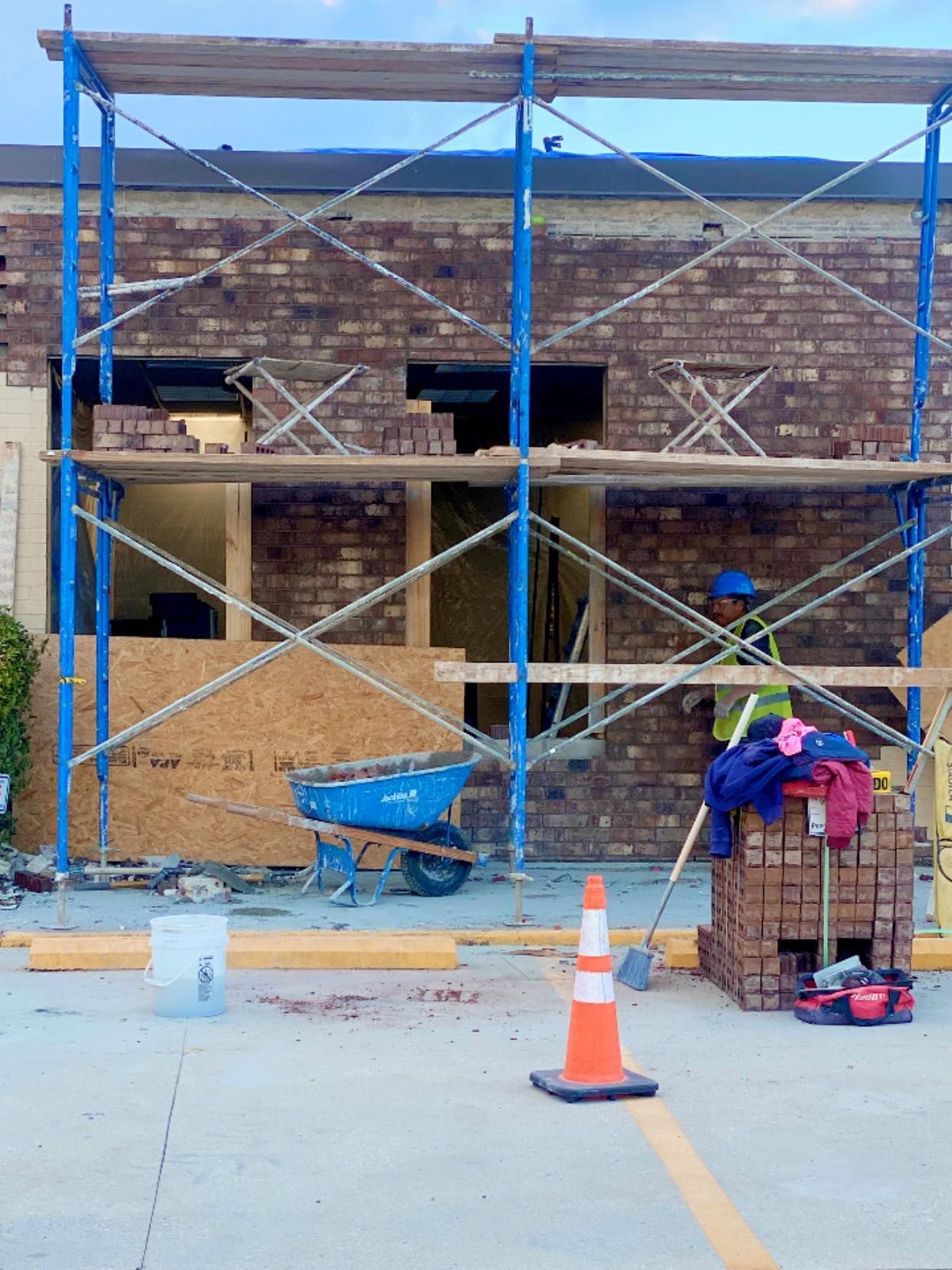 A worker in a high-visibility vest stands by scaffolding and a stack of bricks at a brick-walled building construction site.