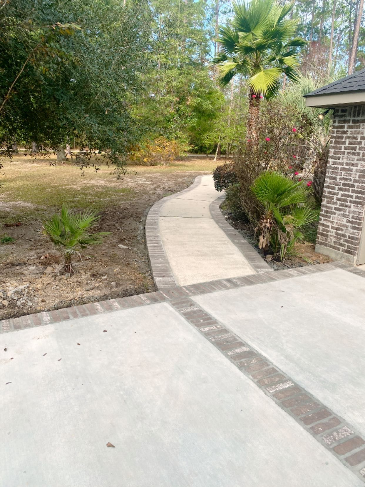 A concrete walkway with a brick border curves through a landscaped yard next to a brick building.