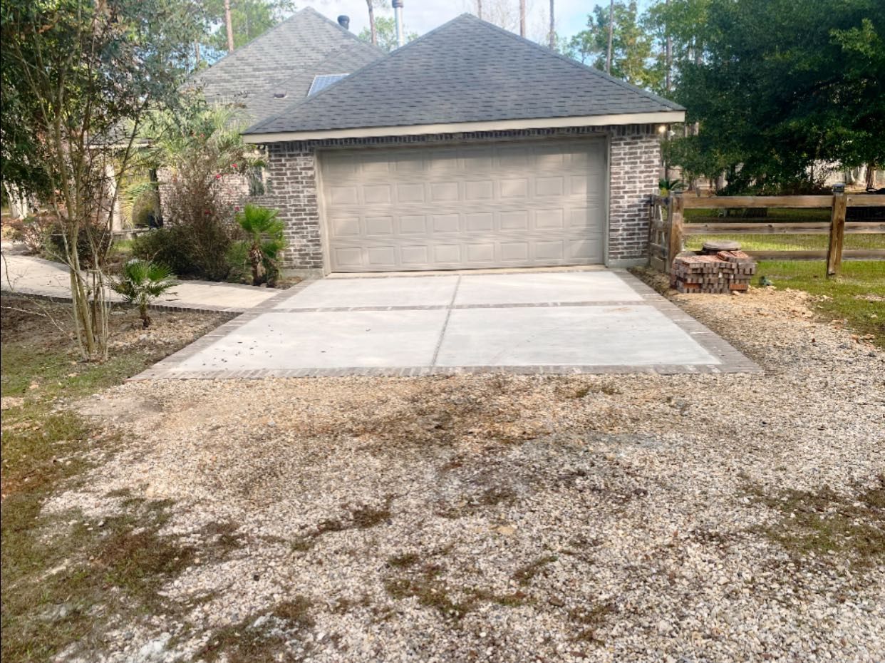 A newly poured light gray concrete driveway apron in front of a tan garage with stone siding and a gray roof.