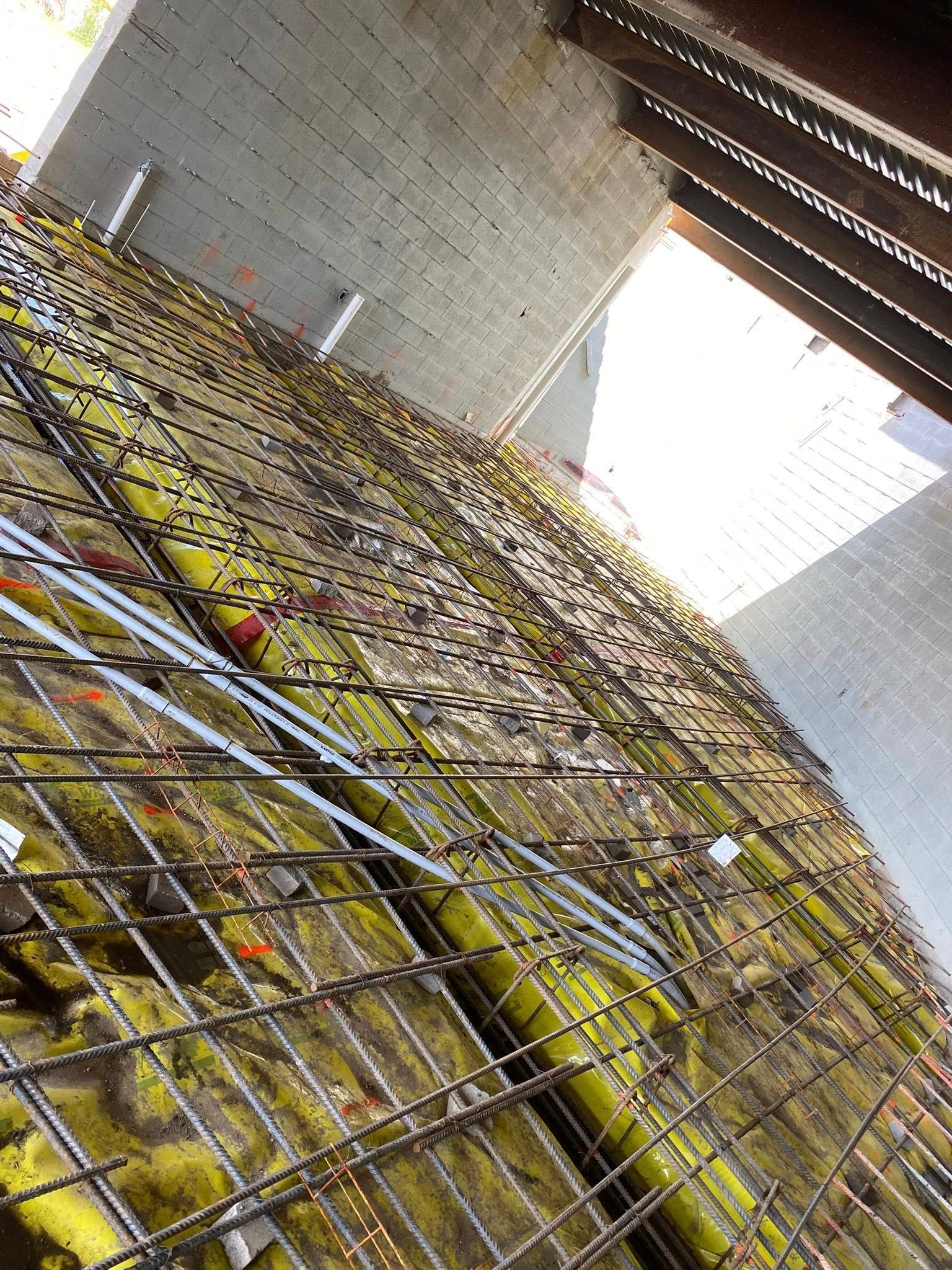 Construction site detail showing a yellow vapor barrier and rebar grid installed on a concrete wall.