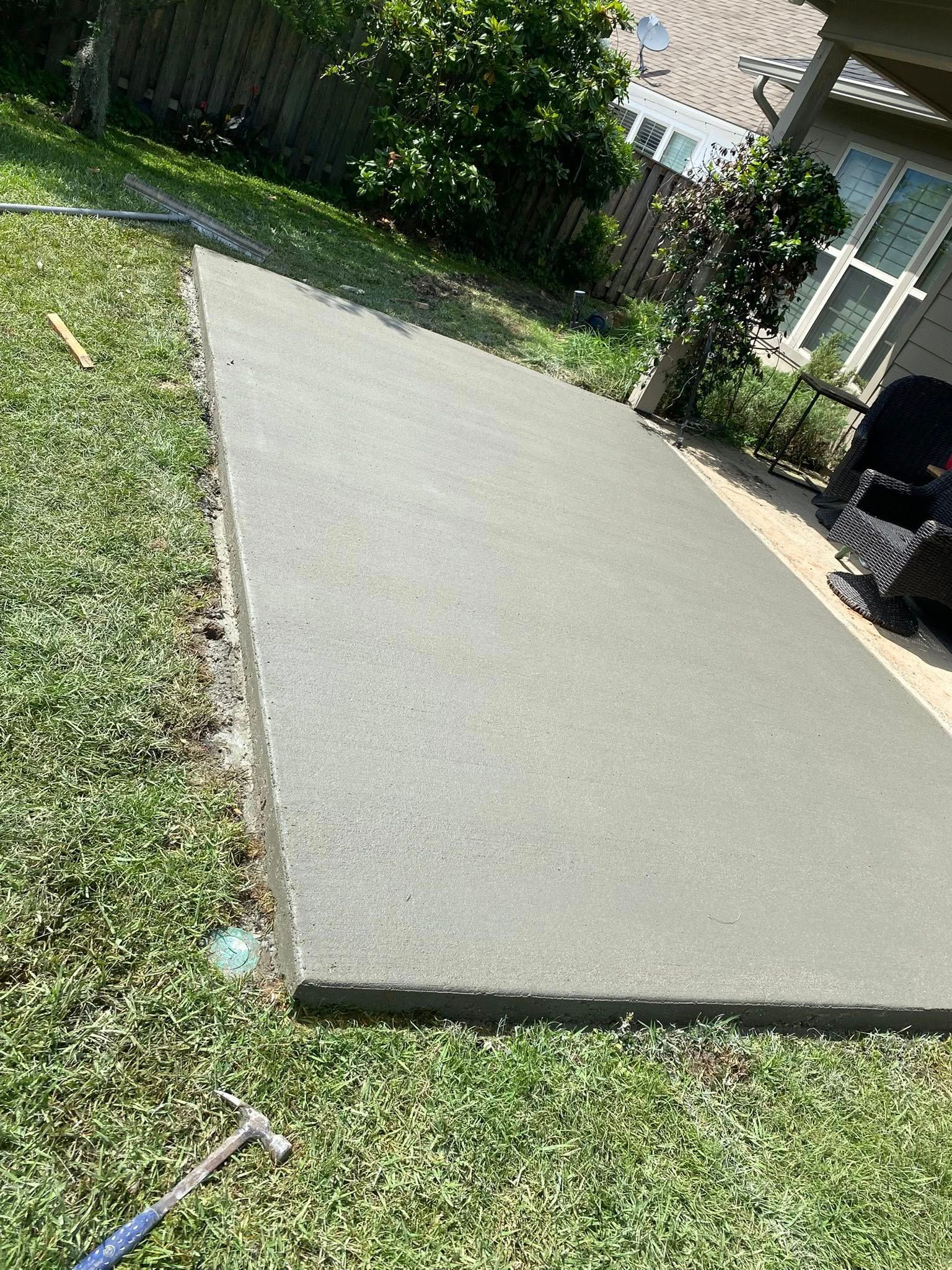 A rectangular concrete slab extension installed in a backyard next to a residential house.