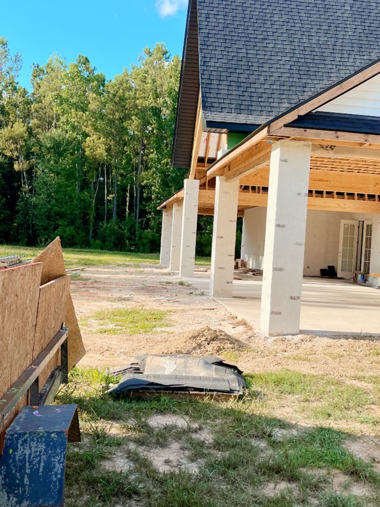 A construction site featuring an unfinished house with a large roofed patio supported by white pillars.