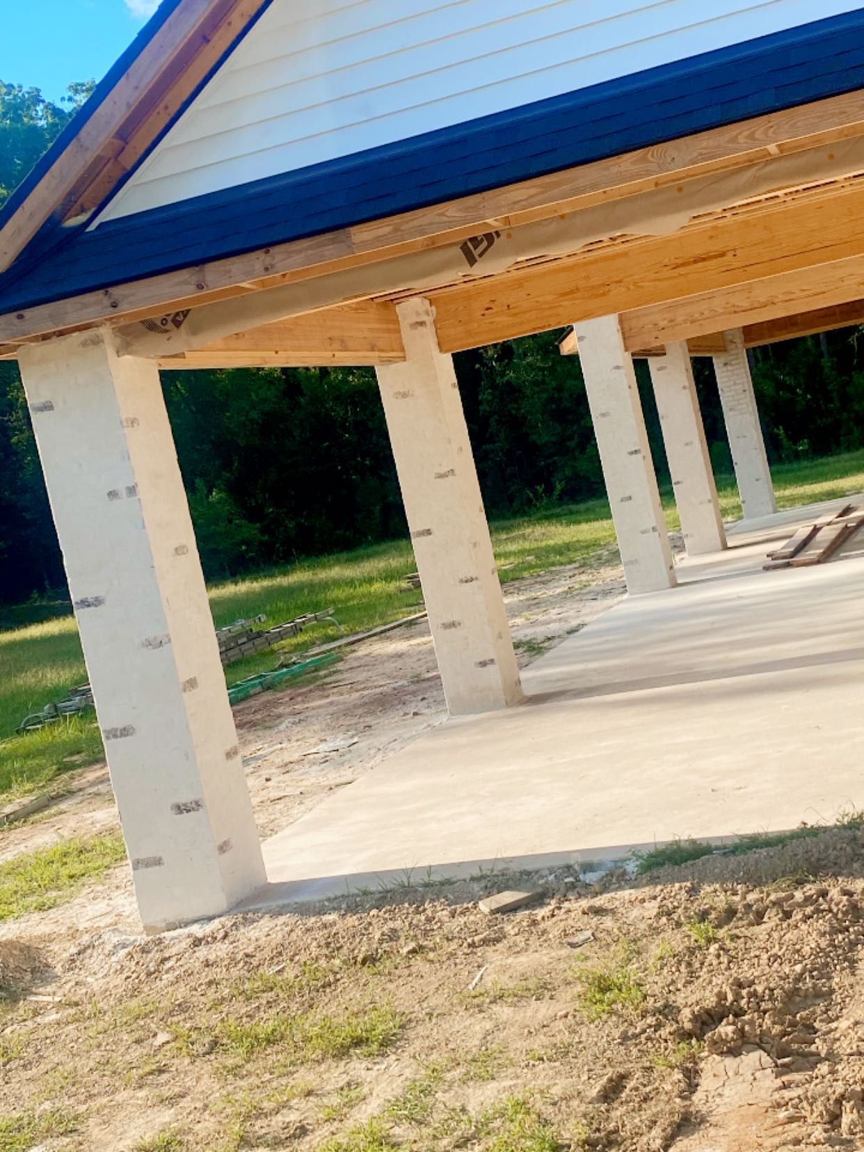 An outdoor structure with a gabled roof supported by square white pillars over a concrete patio.