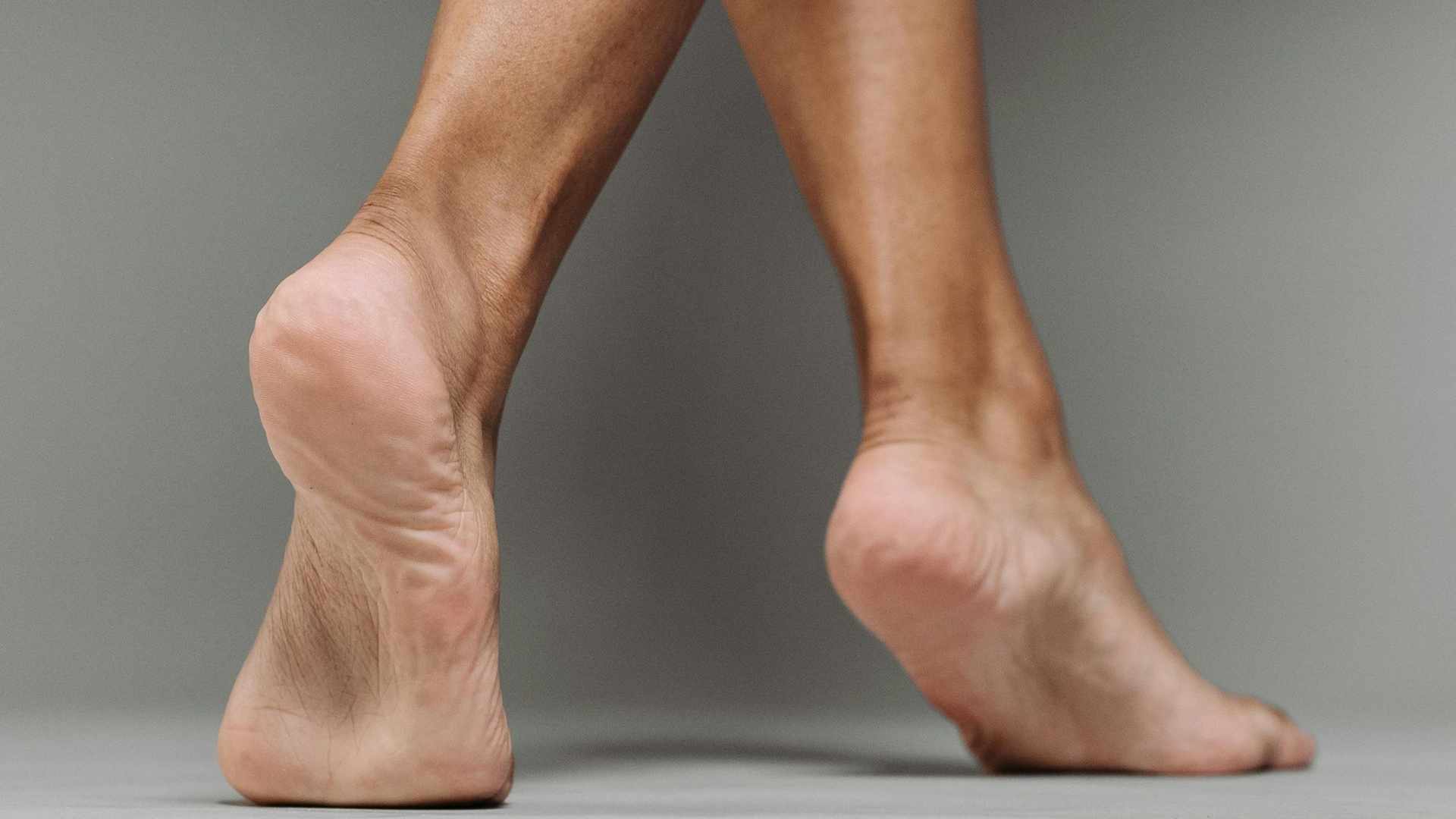 Bare feet, heels raised slightly, against a gray background.