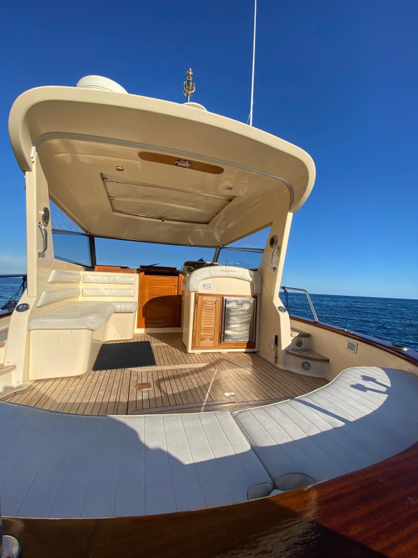 Ponte di poppa dello yacht con tendalino color sabbia, pavimento in legno e vista sull'oceano sotto un cielo azzurro limpido.