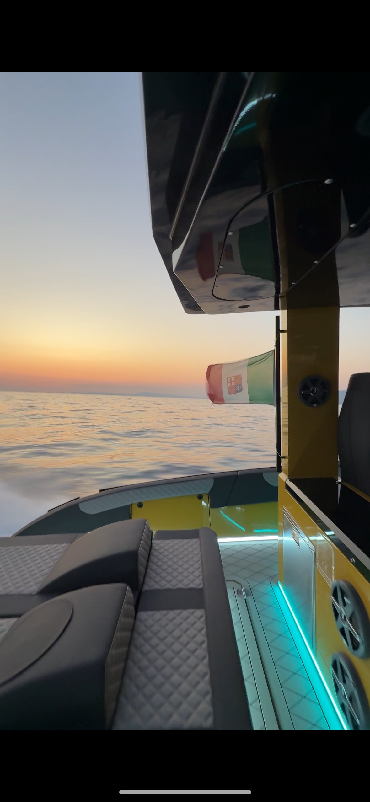 Tramonto su un oceano calmo accanto al ponte di uno yacht con sedute imbottite e luci d'accento blu.