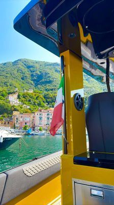 Interno colorato di una barca con vista su un villaggio in riva al lago e verdi colline sotto un sole splendente