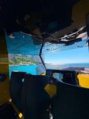 All'interno della cabina di una barca, i sedili offrono una vista sull'acqua turchese e sulla costa lontana attraverso un parabrezza.